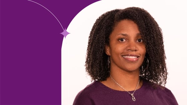 Chavaun standing, using a purple bluse, smiling