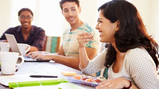 woman eating from a food container at work surrounded by coworkers at a potluck