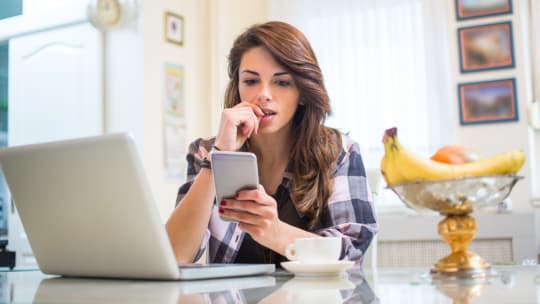 Woman's hands holding iPhone while she's sitting on desk facing laptop