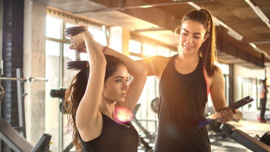 personal trainer holding clipboard while her client lifts a weight