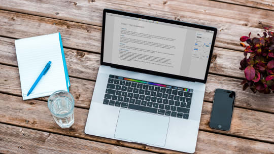 Desk work layout including open laptop, paper notepad with pen, glass of water and phone