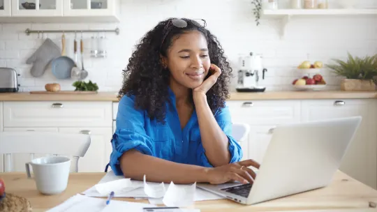 Woman sitting at kitchen desk with laptop in front of her, smiling