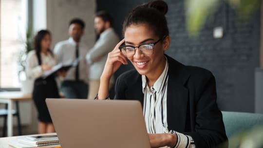 A woman smiles while looking at her laptop