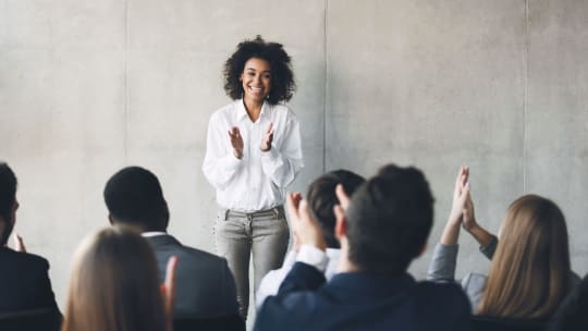 business woman delivering a presentation before a clapping crowd