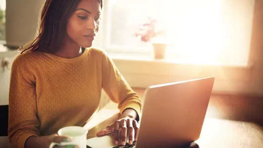 Woman scrolling on laptop with coffee cup in hand.