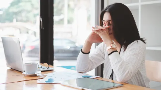 Woman sitting at desk with head in her hands.