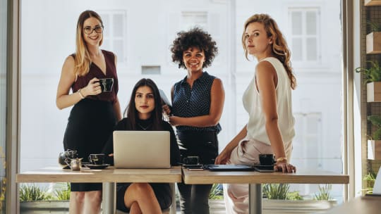 Four women stare into the camera around a table 