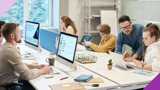 Five people working at an office. One man is explaining something to a woman who looks worried, illustrating why it's important to learn how to deal with competition in the workplace.