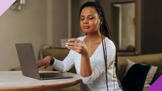 A woman in front of a computer, holding a credit card