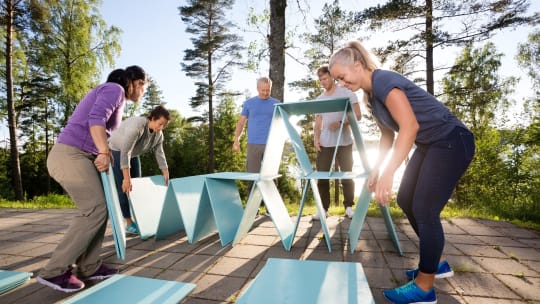 Coworkers Making Pyramid With Blue Planks On Patio