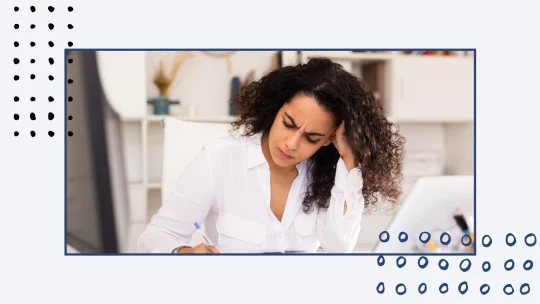 woman with her elbows on the table and her head in her hands, looking distraught, in front of a laptop
