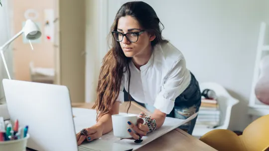 woman leaning over desk looking at laptop