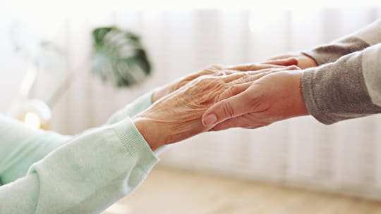 Mature female in elderly care facility gets help from hospital personnel nurse. Senior woman w/ aged wrinkled skin & care giver, hands close up