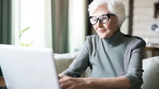 White haired senior woman wearing eyeglasses sitting at cafe and using her laptop