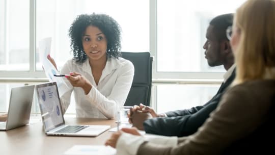 Woman of color pointing to a spreadsheet at a conference table