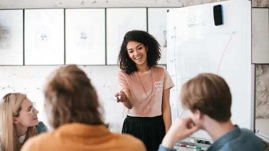 Woman presenting to coworkers in front of a white board.