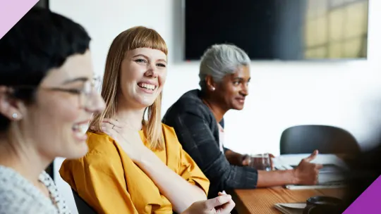 Three coworkers sharing a laugh in an office, illustrating signs of being a people pleaser at work