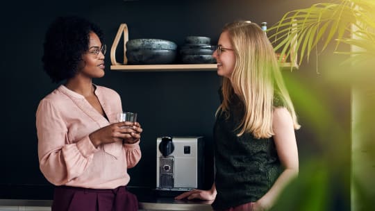 Two women talk in front of an espresso machine
