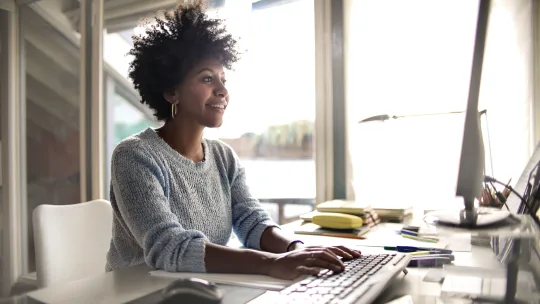 Woman smiling as she types on keyboard and looks up at desktop.