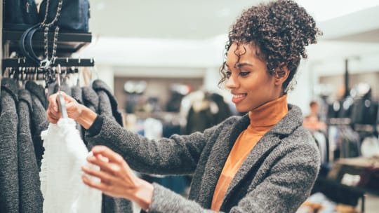 A woman smiles while holding up a top while shopping