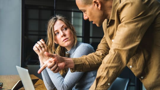 A woman looks up at a man pointing at her laptop