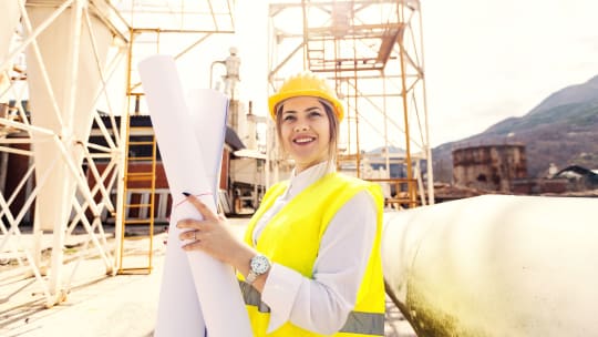 An engineer stands outside while holding blueprints
