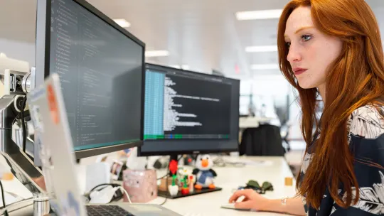 Woman coding on two desktop computers