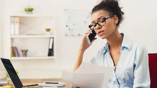 Woman talking on the phone while looking at two pieces of paper.