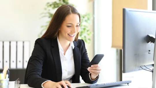 woman checking her phone while sitting at her desk at work