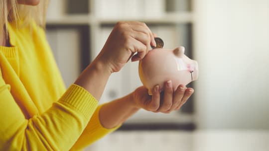 woman dropping a coin into a piggy bank