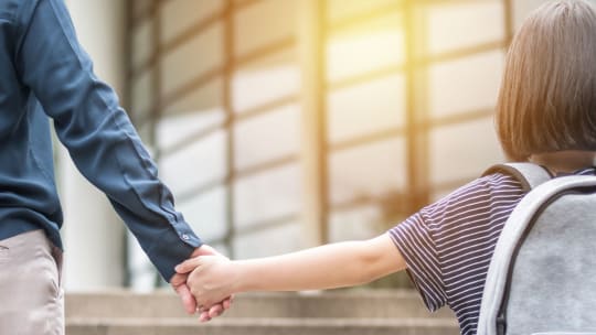 girl with backpack holding her mom's hand