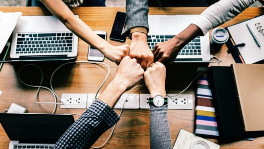 People sitting at a table sharing a collective fist bump 