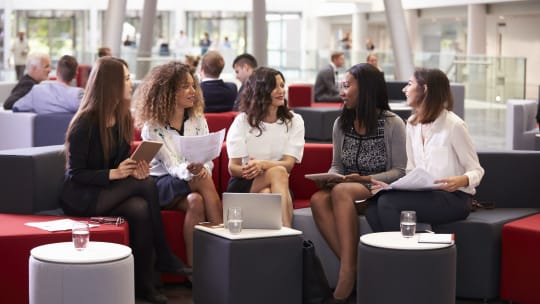 Businesswomen Meeting In Busy Lobby Of Modern Office