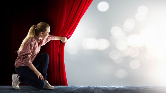 women on stage pulling back curtain