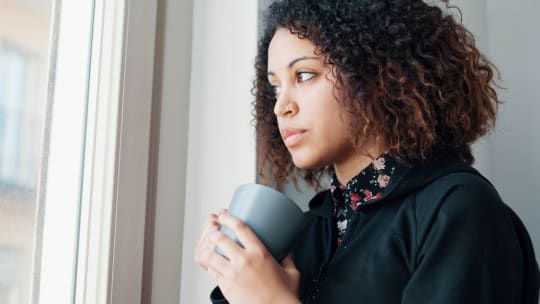 woman with coffee cup in hand looking out window