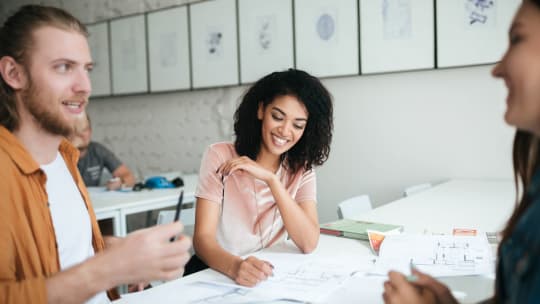 Three coworkers sit at a table interacting