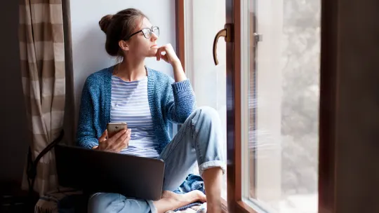 Young woman using laptop and phone in isolation by window