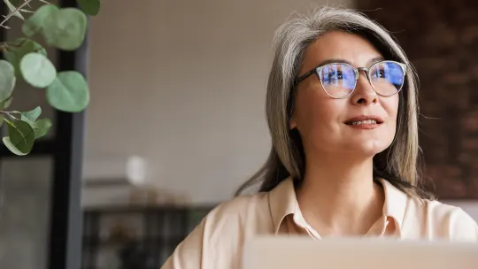 Woman with laptop in front of her looking up left to a window.