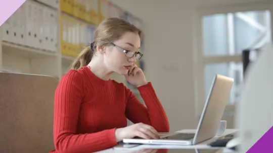 A woman in from of her laptop with a bored face to illustrate why you need to find ways to stay productive when there's nothing to do at work