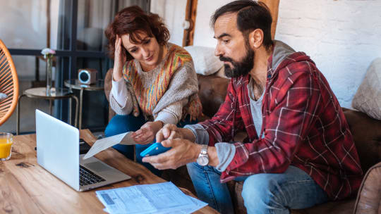 A couple sits at  laptop while looking over documents