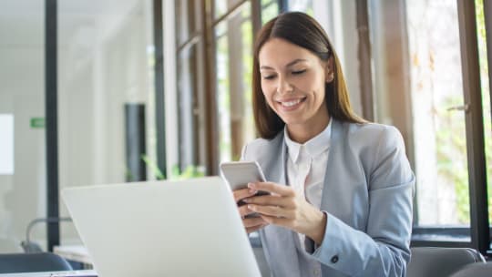 woman sitting at a desk in front of her laptop texting