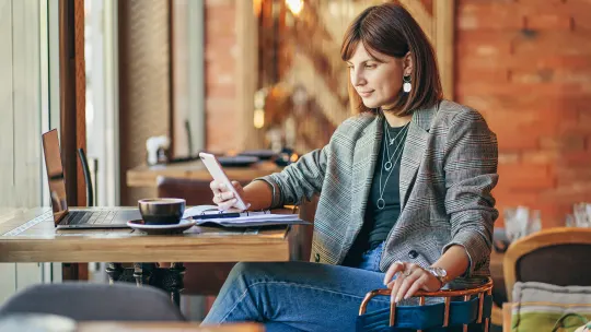 woman sitting at cafe looking at phone and computer