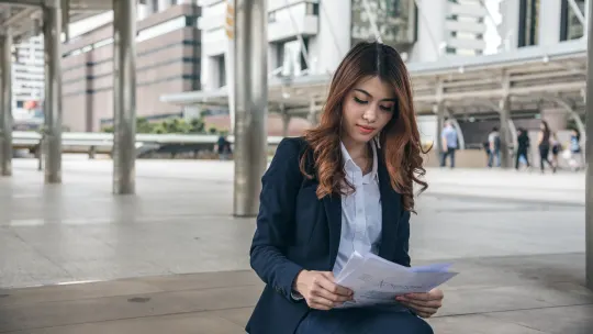 Professional woman sitting outside on bench looking at papers.