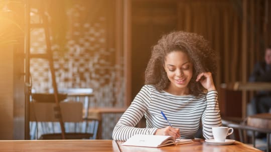 woman writing in a notebook in a coffee shop