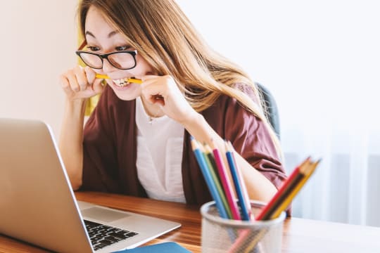 Woman at laptop biting pencil