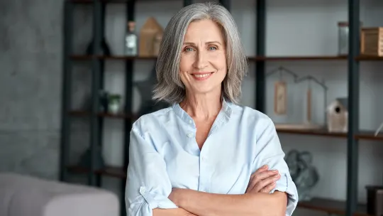 Woman standing with arms crossed, smiling and looking at the camera.