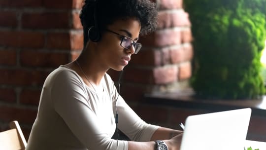 woman with headphones writing on a laptop