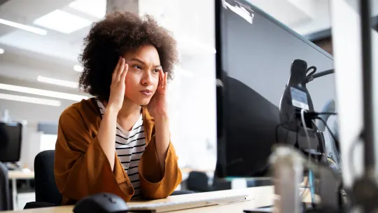 Woman staring frustrated at computer with lips pursed and hands on her temples.