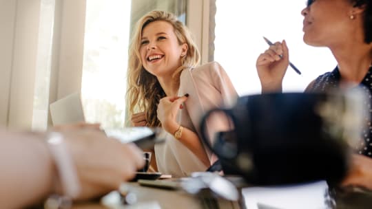 A smiling woman sits at a desk with a blazer thrown over her shoulders