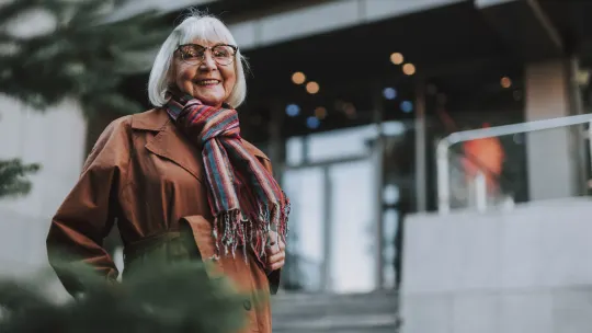 Waist up portrait of charming older woman in coat looking at camera and smiling 